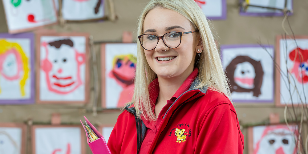 Childcare learner stood in front of a wall of children's paintings