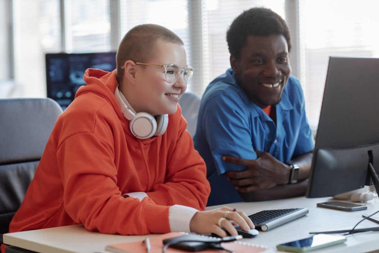 Young, smiling learners working together at a computer screen learning essential skills